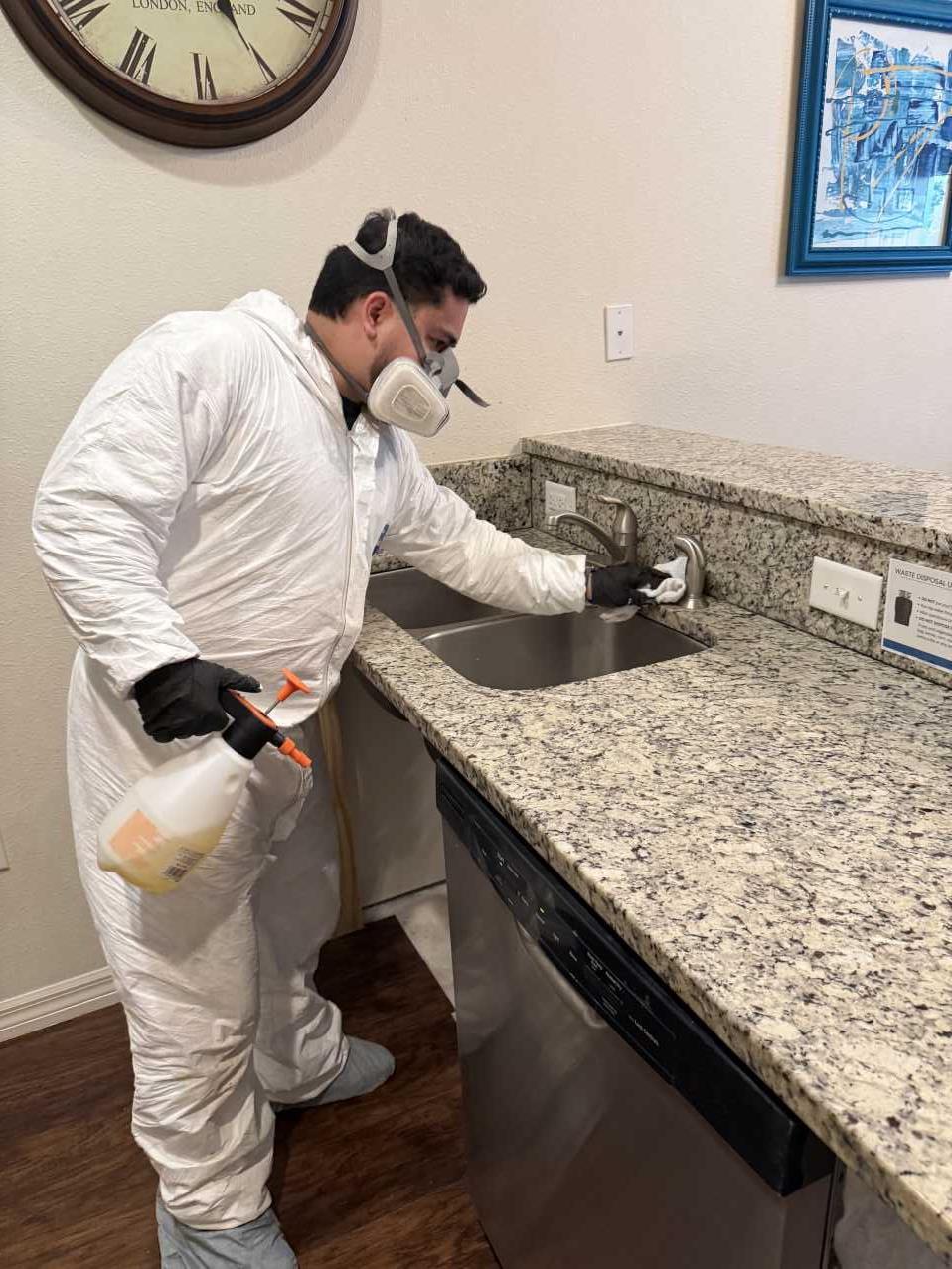 Restoration technician disinfecting countertop and sink surfaces during commercial mold cleanup