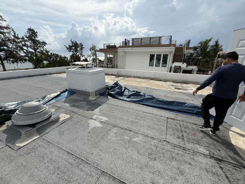 Crew member laying a heavy-duty tarp across a commercial flat roof