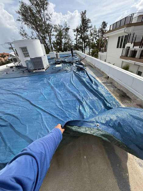 Restoration crew member securing and tightening a roof tarp during emergency tarping