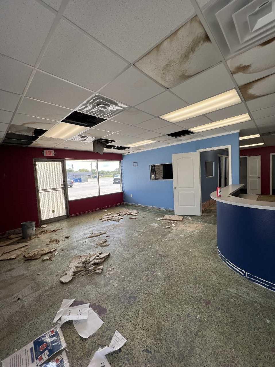 Commercial office interior with storm-damaged ceiling tiles and debris before restoration