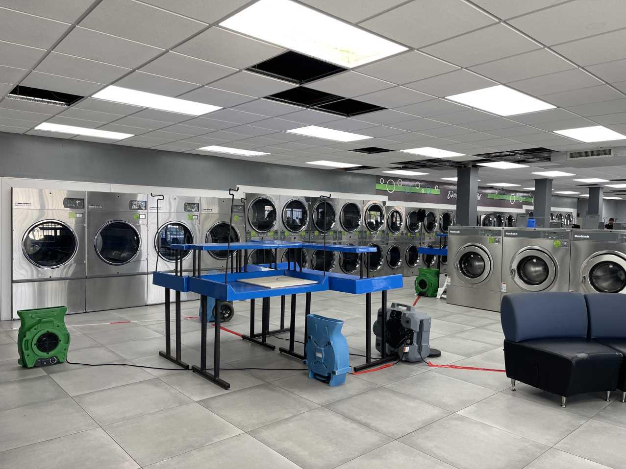 Wide view of commercial laundromat drying equipment and damaged ceiling tiles