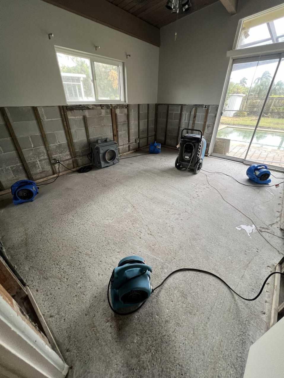Air movers and dehumidifiers drying a Florida living room after Hurricane Helene flooding