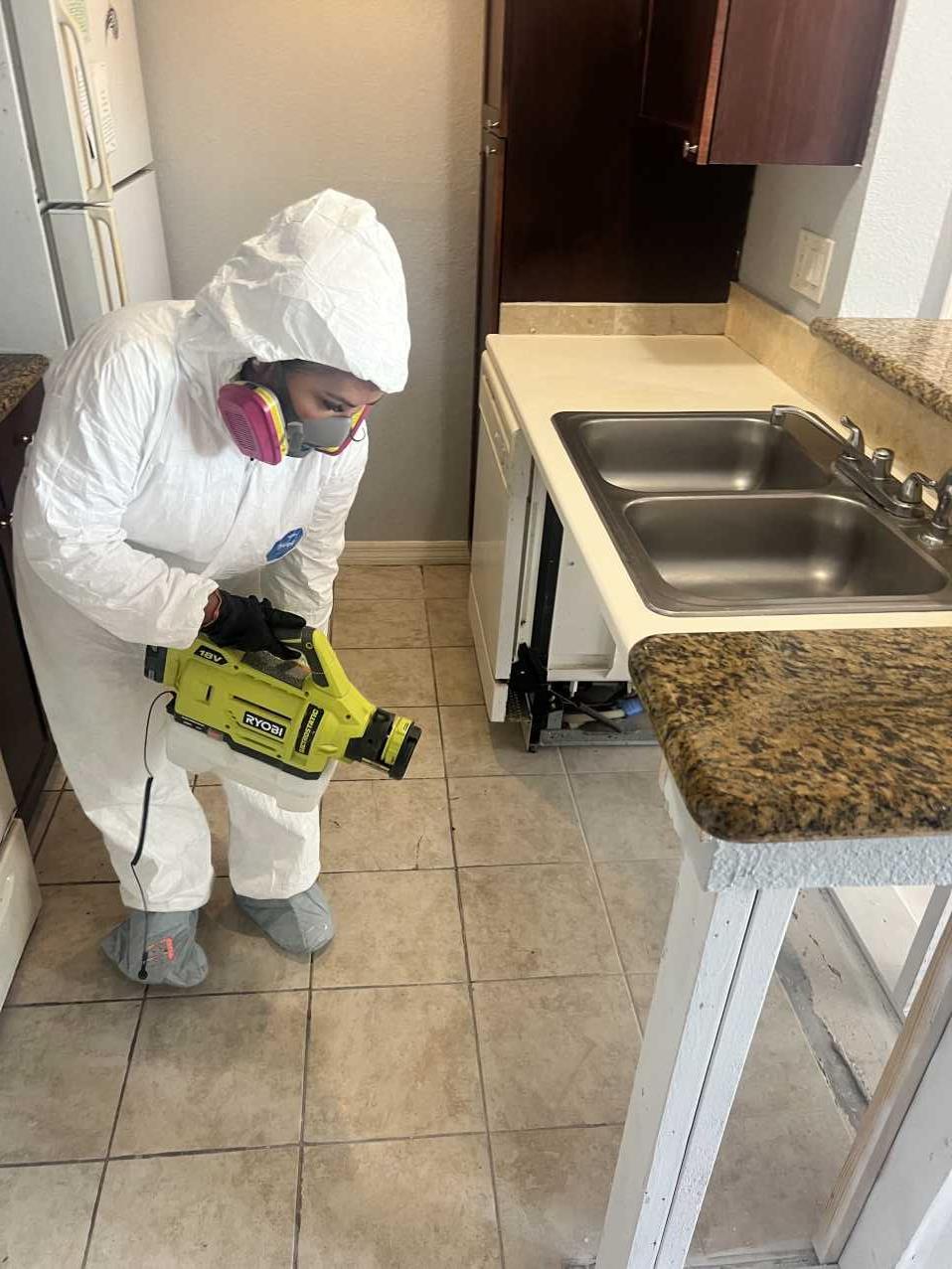 Restoration technician applying antimicrobial treatment under a kitchen sink during mold remediation