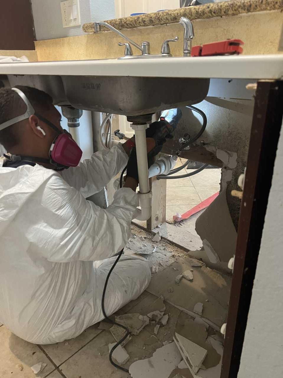 Restoration technician working on plumbing under a kitchen sink during mold remediation