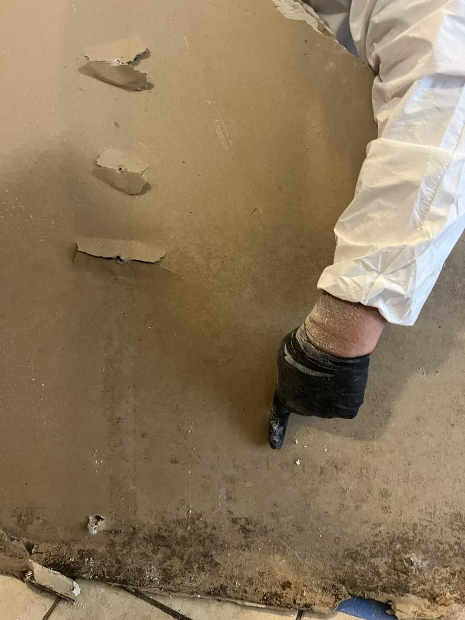 Restoration technician scraping mold-affected material from a kitchen floor