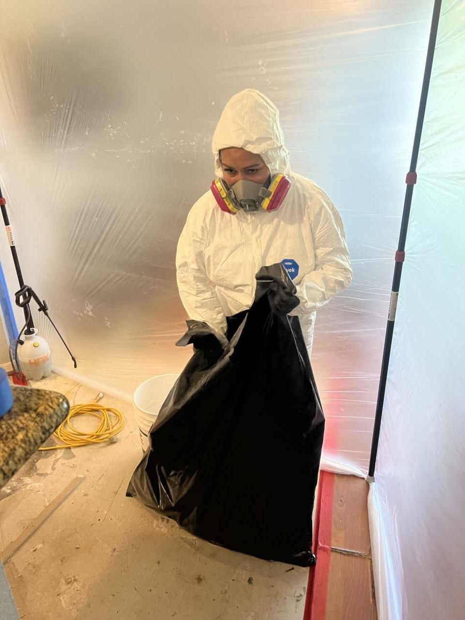Restoration technician removing mold-affected waste material during remediation