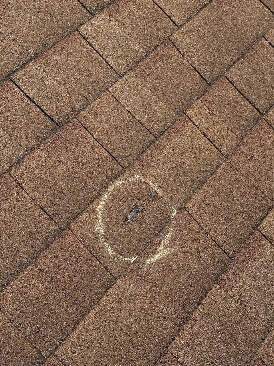 Close-up of a marked impact point on a shingle roof during storm damage inspection