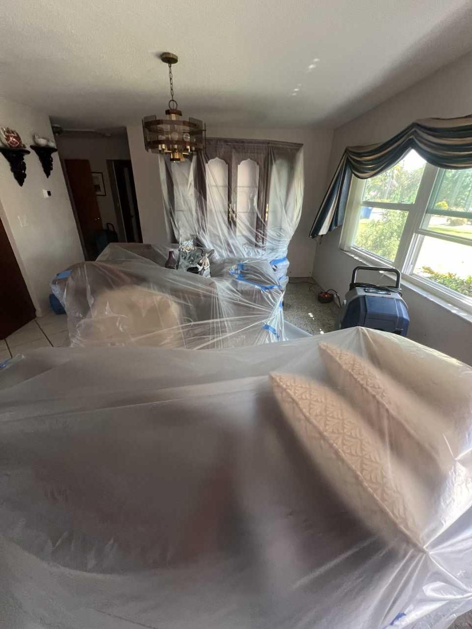 Dining room furniture wrapped in plastic with a dehumidifier running during storm restoration