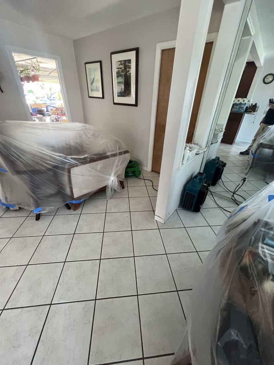 Furniture wrapped in plastic with air movers running during storm damage restoration