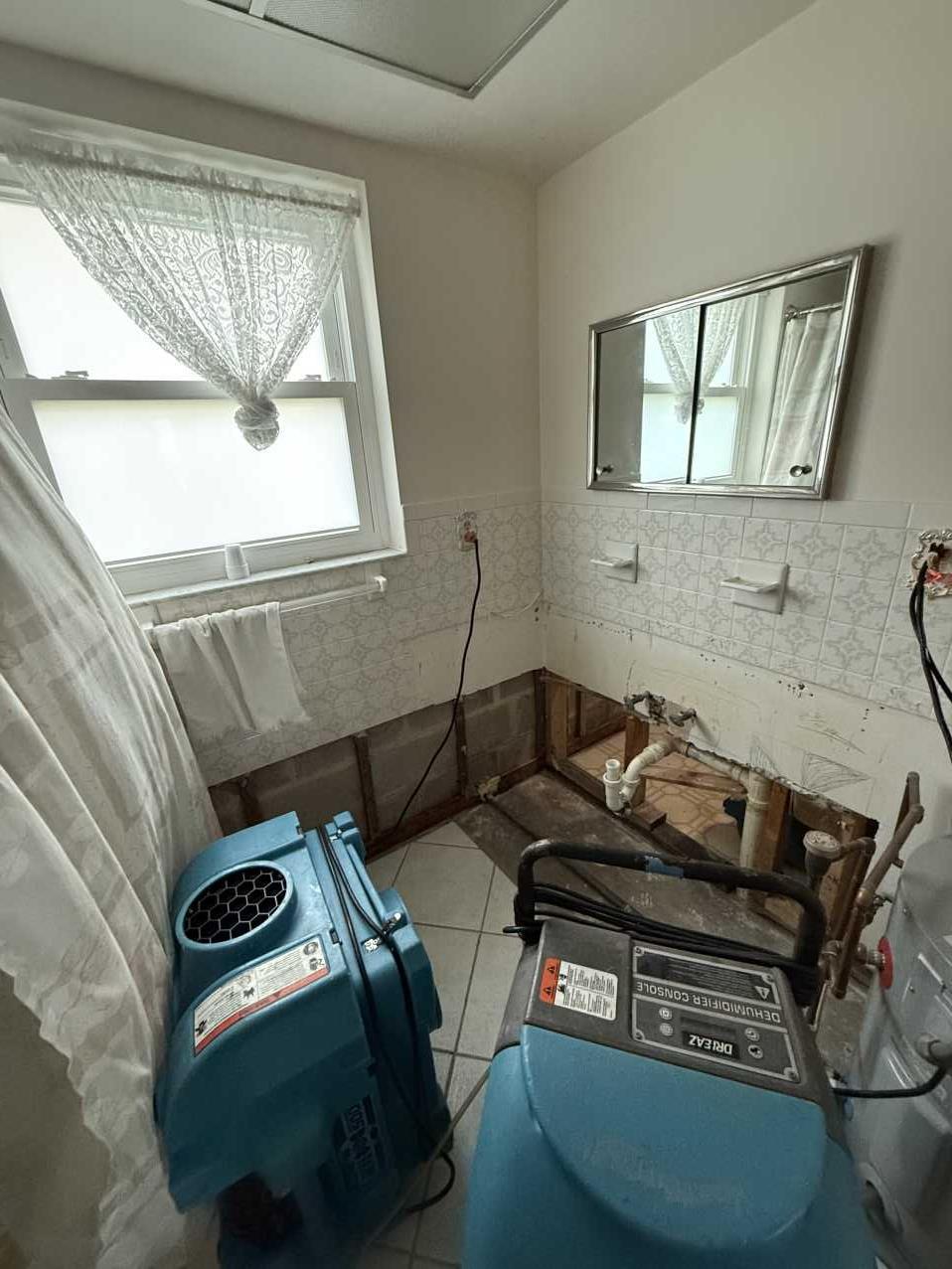 Bathroom with flood cut drywall exposing studs and drying equipment running
