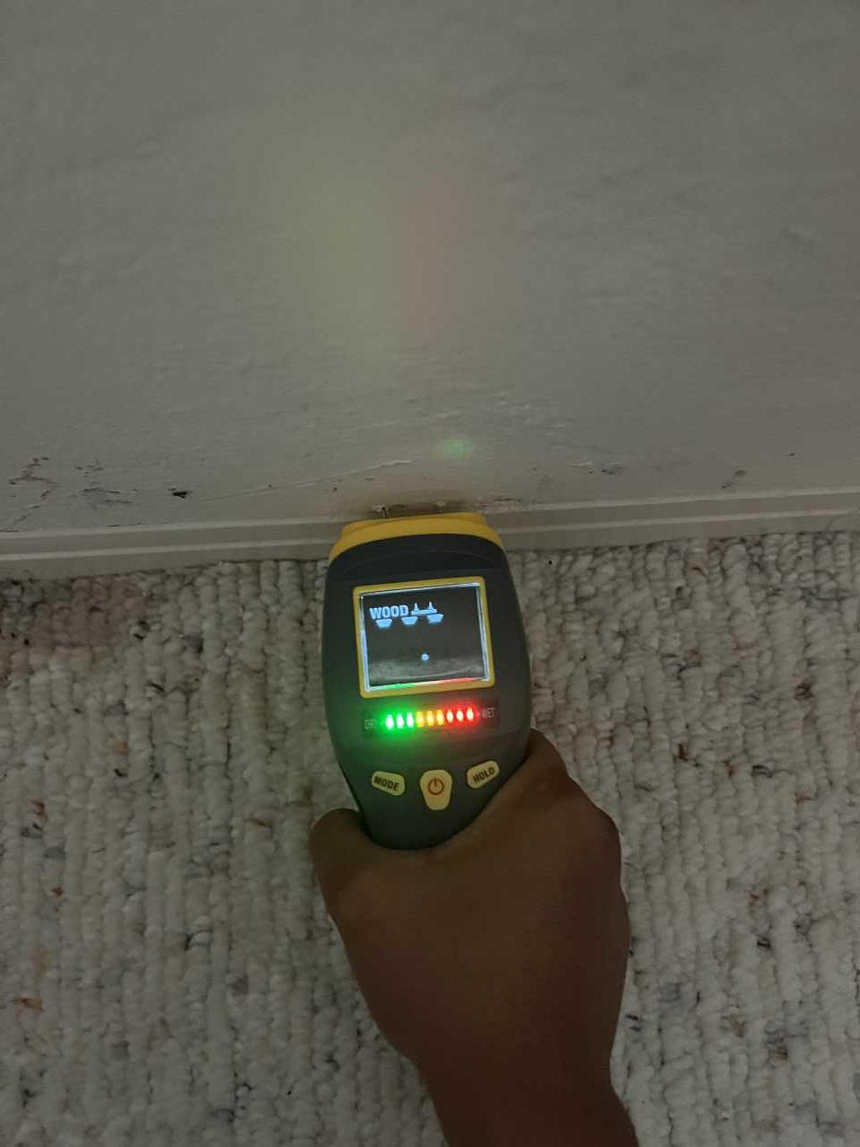 Moisture meter showing a wet reading on wood baseboard during storm damage inspection