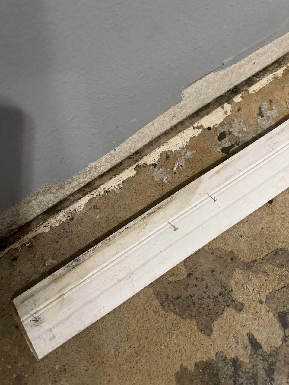 Close-up of water-damaged baseboard trim and flooring from a burst pipe