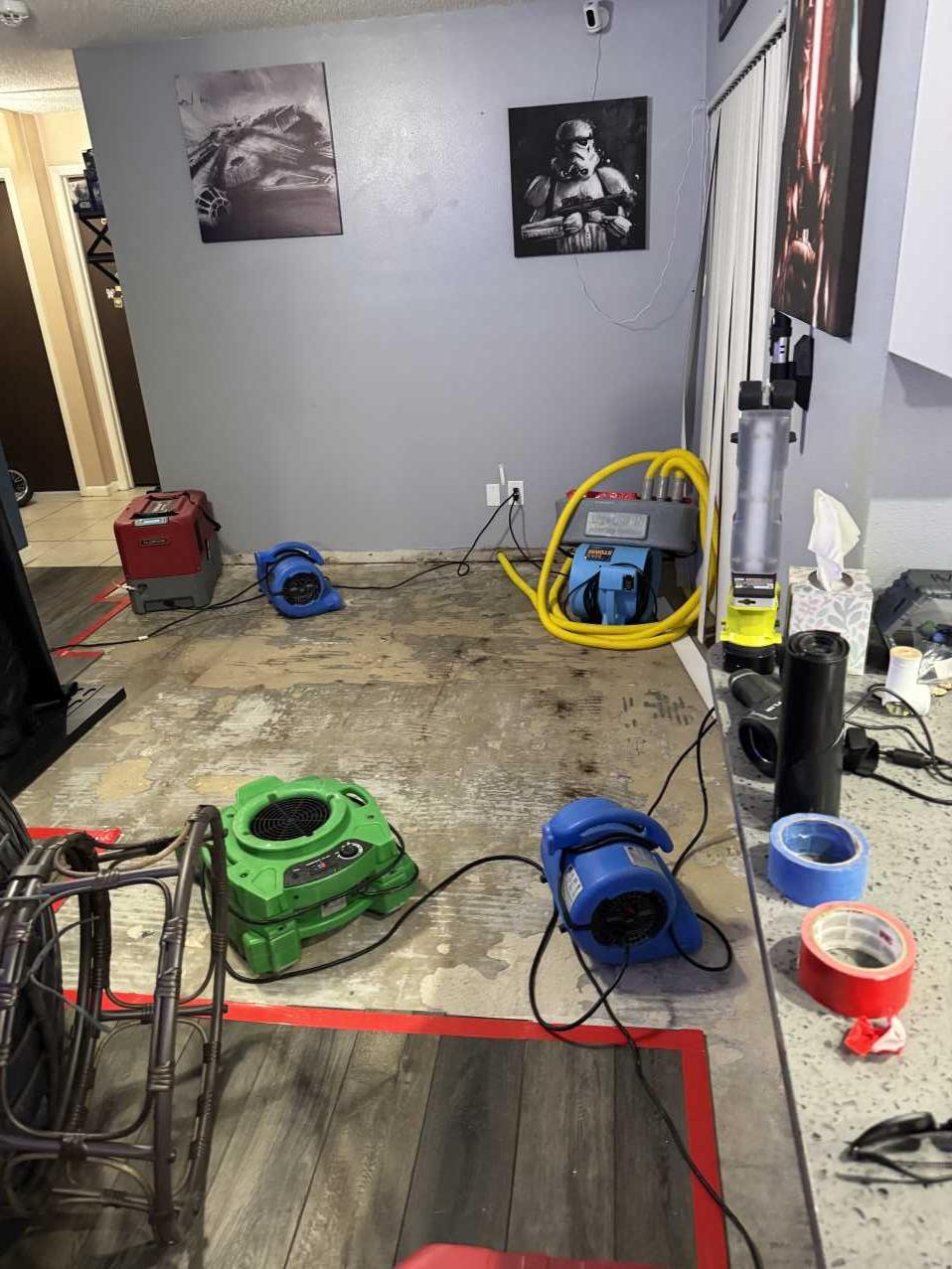 Air movers and a dehumidifier drying a living room floor after water damage spread from a bathroom