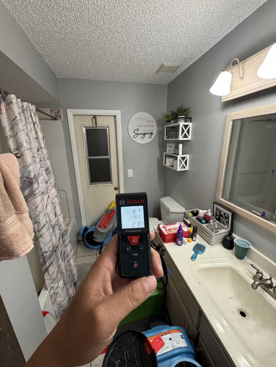 Restoration technician taking laser measurements of a bathroom during water damage documentation